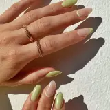 Delikatny manicure naturalny z pastelowo-zielonym akcentem na końcówkach. Dłonie ozdobione złotymi pierścionkami.