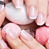Elegancki manicure francuski na zadbanych dłoniach, otoczony różowymi i białymi ozdobami. To kwintesencja klasyki, czyli co to manicure.