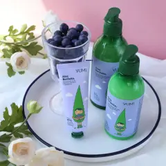 Krem do rąk i balsam do ciała YUMI Aloe Borówka, z uroczą grafiką, obok szklanki jagód i kwiatów.