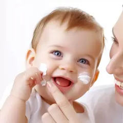 Uśmiechnięte dziecko z białymi plamkami sudocremu na twarzy, mama delikatnie dotyka jego policzka.