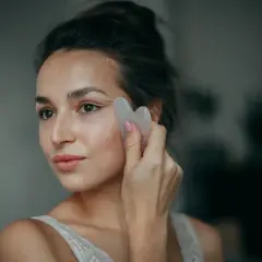 Kobieta wykonuje masaż twarzy kamieniem gua sha, zastanawiając się, czy lepszy jest masaż gua sha rano czy wieczorem.