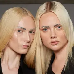 Dwie modelki o żółtym blond włosach i błyszczących brwiach z brokatem.