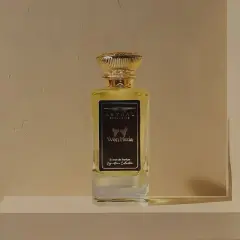 Elegancka butelka perfum "Won Hedia" z nutami kadzidła, w złotym korku, na tle teksturowanej ściany.