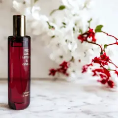 Czerwona butelka perfum Red Zara Temptation & Vanilla, z kwiatami w tle. Idealny odpowiednik dla miłośniczek słodkich, zmysłowych zapachów.
