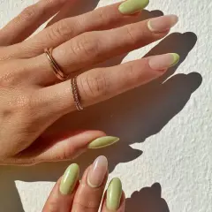Delikatny manicure naturalny z pastelowo-zielonym akcentem na końcówkach. Dłonie ozdobione złotymi pierścionkami.