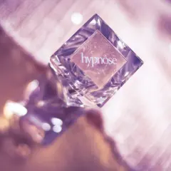 Szklana buteleczka perfum "hypnose" na różowym, błyszczącym tle.
