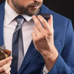 Elegancki mężczyzna w niebieskiej marynarce wącha perfumy. Zapach, niczym karnozyna, dodaje mu pewności siebie.