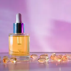Szklana buteleczka z serum i kapsułki na fioletowym tle. Wybór między retinol czy retinal dla pięknej skóry.