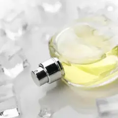 Szklana buteleczka perfum z żółtym płynem, otoczona kostkami lodu. Zapach niczym orzeźwiający szypr.