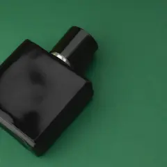 Elegancka, czarna butelka perfum z nutami **vetiver** na zielonym tle.