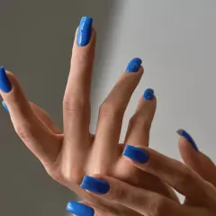Dłonie z idealnym, letnim manicure w odcieniu kobaltowego błękitu. Paznokcie są długie, kwadratowe i błyszczące.