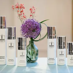 Linia kosmetyków MBR: Premium Cleanser, Face Mask, Face Serum, Face Cream, Eye Cream i Lip-ID, obok fioletowego czosnku i drobnych różowych kwiatów.