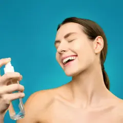 Uśmiechnięta kobieta rozpyla na twarz hydrolat. To naturalny tonik, który odświeża i nawilża skórę.