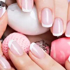Elegancki manicure francuski na zadbanych dłoniach, otoczony różowymi i białymi ozdobami. To kwintesencja klasyki, czyli co to manicure.