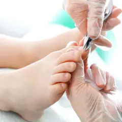 Delikatne dłonie w rękawiczkach precyzyjnie obcinają paznokcie u nóg, dbając o każdy szczegół.