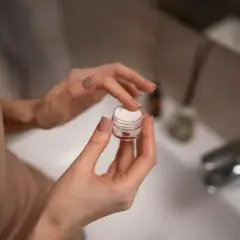 Dłonie nabierają krem z retinolem 0,1% z małego słoiczka, przygotowując się do wieczornej pielęgnacji.