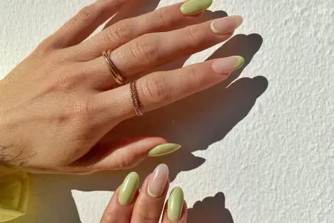 Delikatny manicure naturalny z pastelowo-zielonym akcentem na końcówkach. Dłonie ozdobione złotymi pierścionkami.