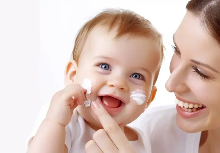 Uśmiechnięte dziecko z białymi plamkami sudocremu na twarzy, mama delikatnie dotyka jego policzka.