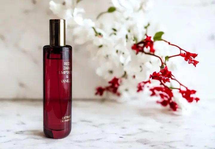 Czerwona butelka perfum Red Zara Temptation & Vanilla, z kwiatami w tle. Idealny odpowiednik dla miłośniczek słodkich, zmysłowych zapachów.