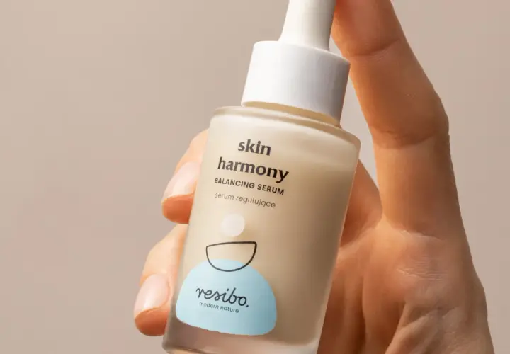 Dłoń trzyma buteleczkę serum Resibo z alantoiną, które koi i nawilża skórę.