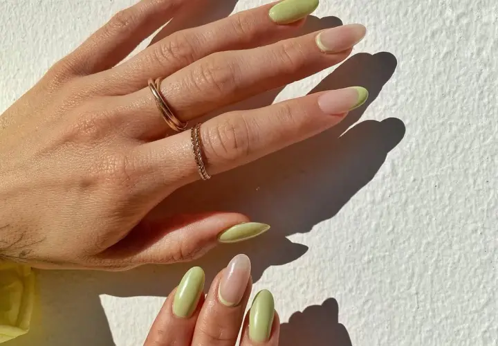 Delikatny manicure naturalny z pastelowo-zielonym akcentem na końcówkach. Dłonie ozdobione złotymi pierścionkami.