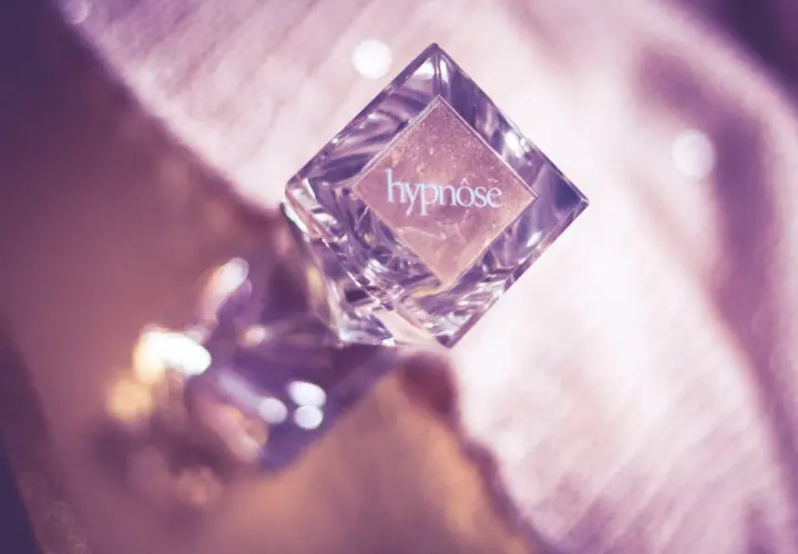 Szklana buteleczka perfum "hypnose" na różowym, błyszczącym tle.