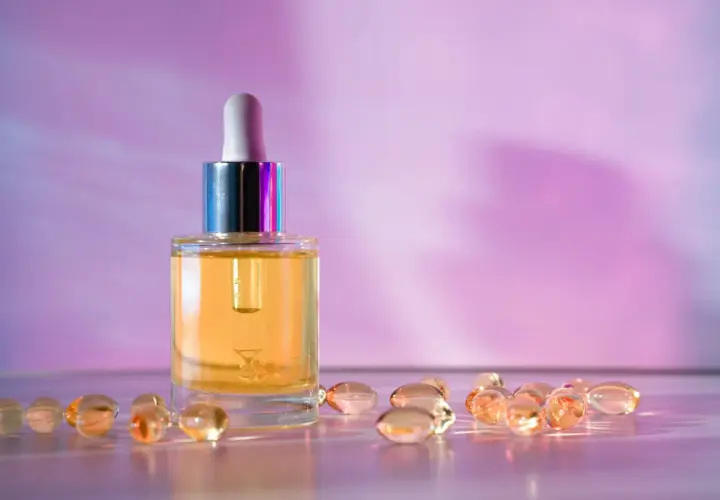 Szklana buteleczka z serum i kapsułki na fioletowym tle. Wybór między retinol czy retinal dla pięknej skóry.