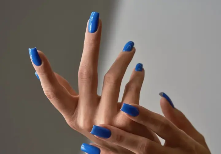 Dłonie z idealnym, letnim manicure w odcieniu kobaltowego błękitu. Paznokcie są długie, kwadratowe i błyszczące.