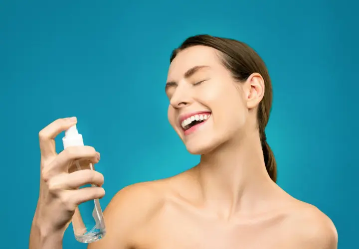 Uśmiechnięta kobieta rozpyla na twarz hydrolat. To naturalny tonik, który odświeża i nawilża skórę.