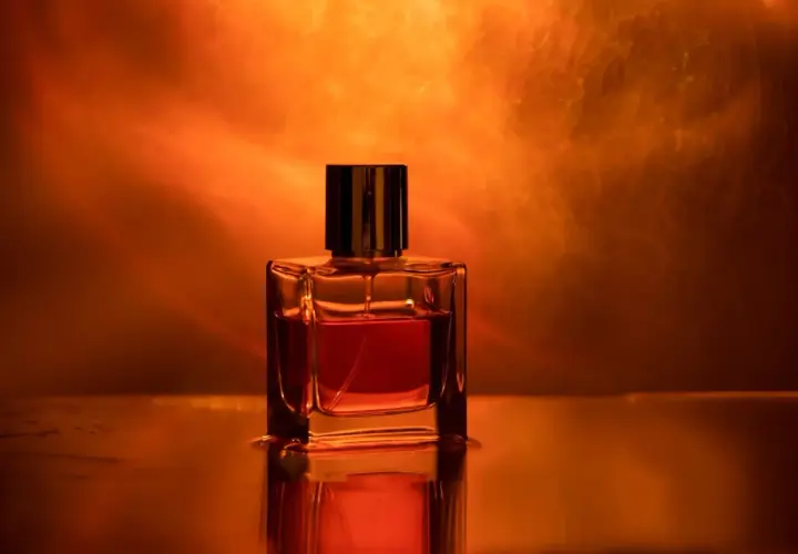 Szklana buteleczka perfum z bursztynowym płynem, otoczona ciepłym, pomarańczowym światłem. Ten zapach to obietnica luksusu.