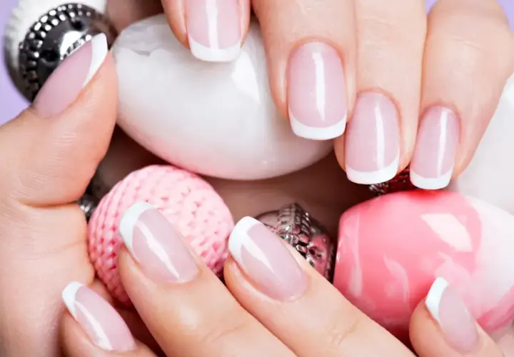 Elegancki manicure francuski na zadbanych dłoniach, otoczony różowymi i białymi ozdobami. To kwintesencja klasyki, czyli co to manicure.