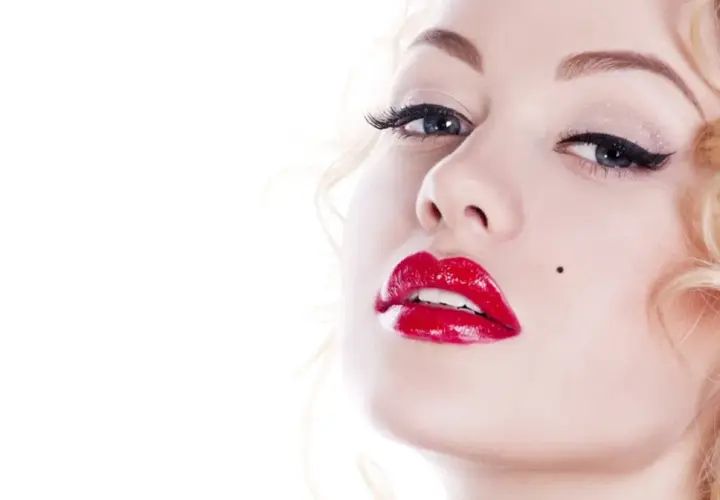 Kobieta z burzą blond loków i charakterystycznym pieprzykiem, usta w stylu Marilyn Monroe, błyszczące czerwone.