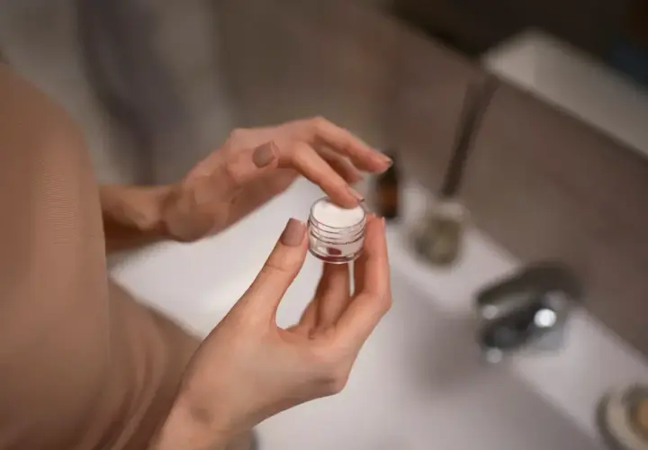 Dłonie nabierają krem z retinolem 0,1% z małego słoiczka, przygotowując się do wieczornej pielęgnacji.
