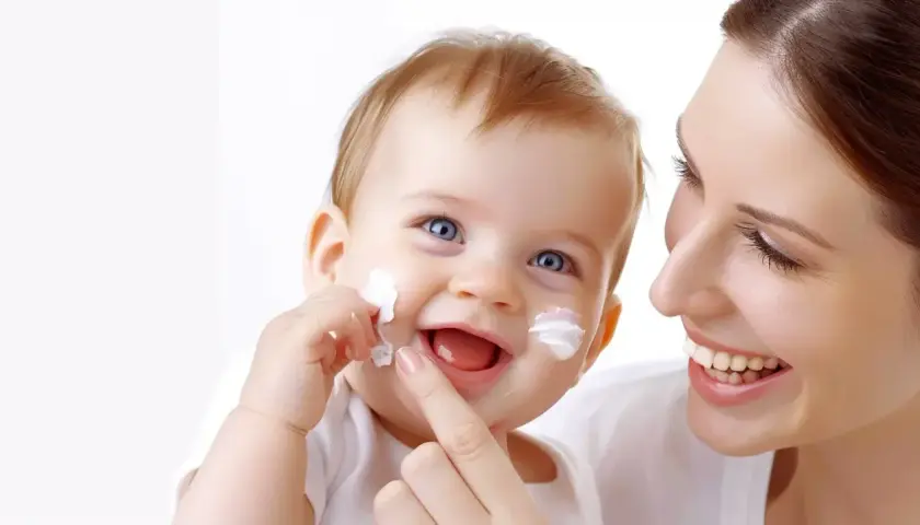 Uśmiechnięte dziecko z białymi plamkami sudocremu na twarzy, mama delikatnie dotyka jego policzka.