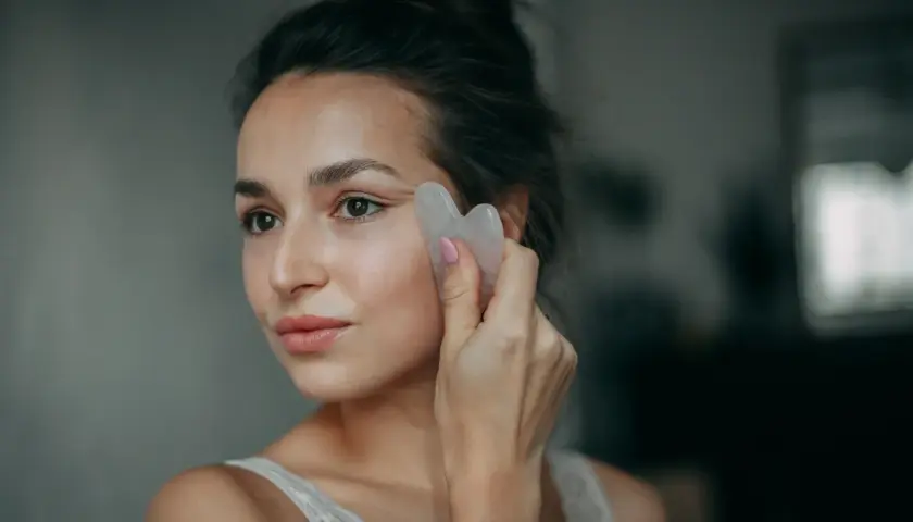 Kobieta wykonuje masaż twarzy kamieniem gua sha, zastanawiając się, czy lepszy jest masaż gua sha rano czy wieczorem.