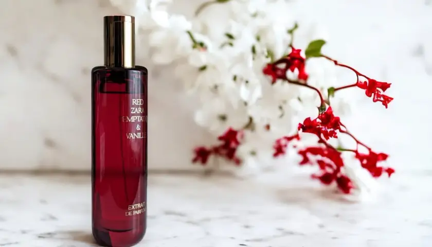 Czerwona butelka perfum Red Zara Temptation & Vanilla, z kwiatami w tle. Idealny odpowiednik dla miłośniczek słodkich, zmysłowych zapachów.