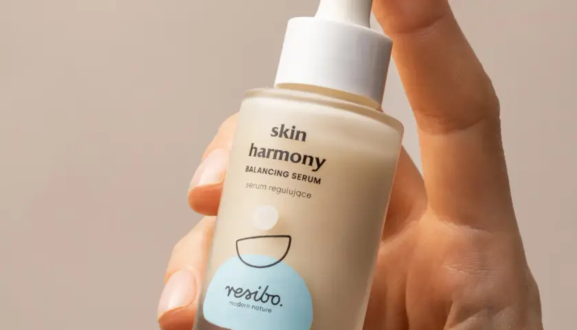 Dłoń trzyma buteleczkę serum Resibo z alantoiną, które koi i nawilża skórę.