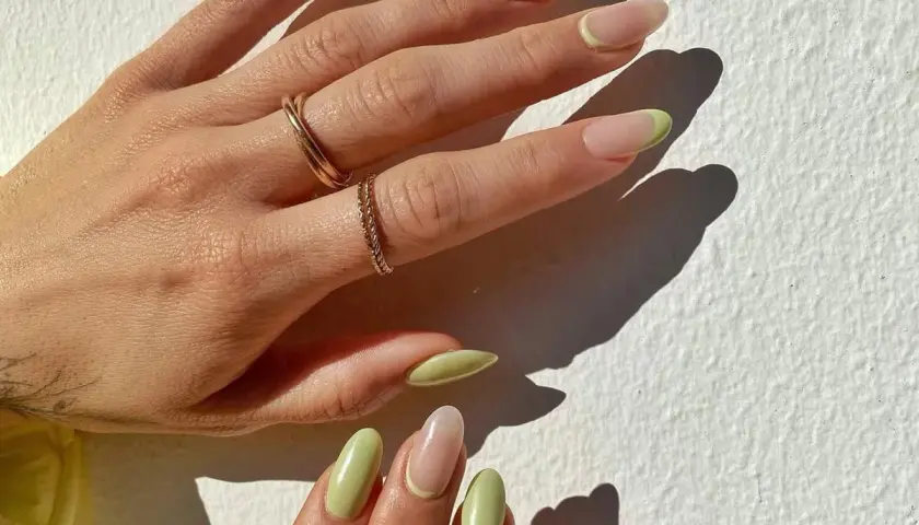 Delikatny manicure naturalny z pastelowo-zielonym akcentem na końcówkach. Dłonie ozdobione złotymi pierścionkami.