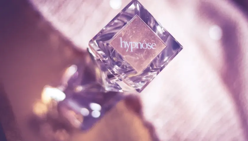 Szklana buteleczka perfum "hypnose" na różowym, błyszczącym tle.