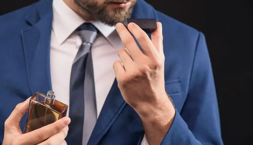 Elegancki mężczyzna w niebieskiej marynarce wącha perfumy. Zapach, niczym karnozyna, dodaje mu pewności siebie.