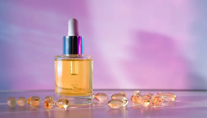 Szklana buteleczka z serum i kapsułki na fioletowym tle. Wybór między retinol czy retinal dla pięknej skóry.