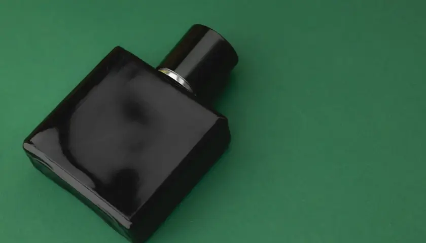 Elegancka, czarna butelka perfum z nutami **vetiver** na zielonym tle.