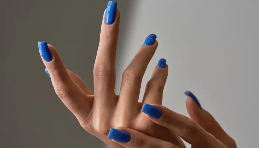 Dłonie z idealnym, letnim manicure w odcieniu kobaltowego błękitu. Paznokcie są długie, kwadratowe i błyszczące.
