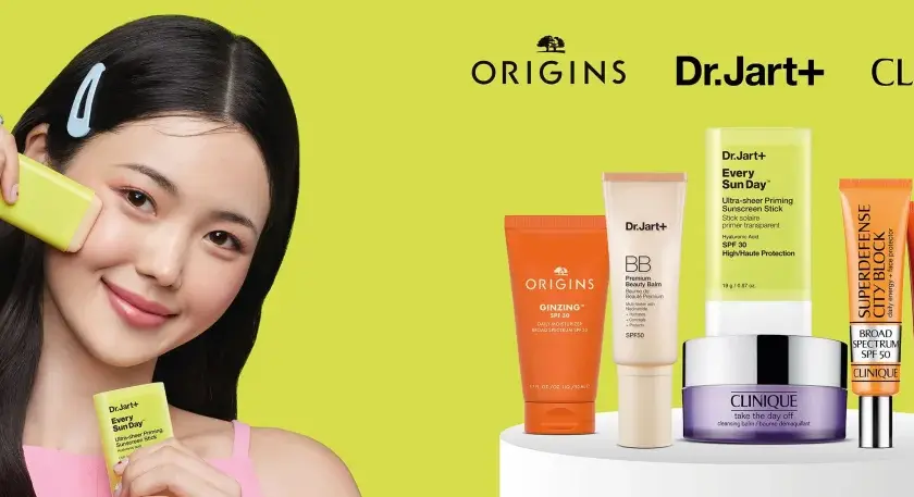 Młoda kobieta aplikuje na twarz kosmetyk z filtrem SPF. Obok niej produkty Origins, Dr.Jart+ i Clinique, pomagające wybrać jaki SPF do twarzy będzie najlepszy.