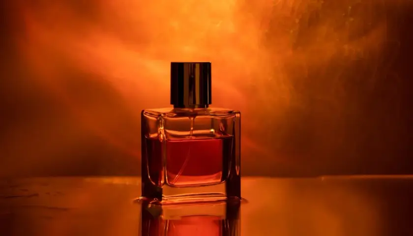 Szklana buteleczka perfum z bursztynowym płynem, otoczona ciepłym, pomarańczowym światłem. Ten zapach to obietnica luksusu.