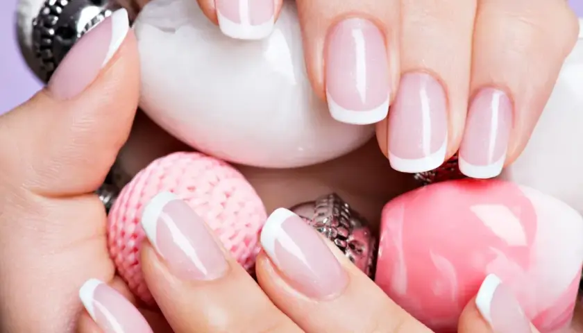 Elegancki manicure francuski na zadbanych dłoniach, otoczony różowymi i białymi ozdobami. To kwintesencja klasyki, czyli co to manicure.