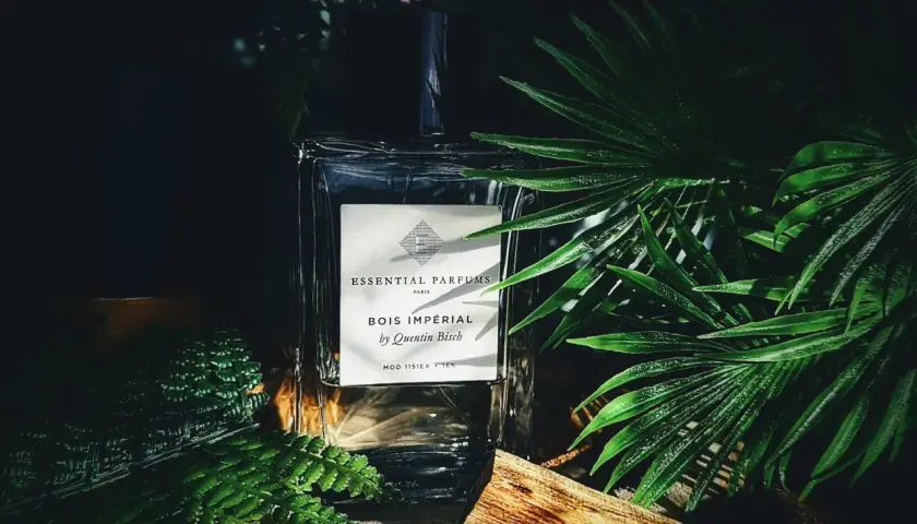 Elegancka butelka perfum Bois Impérial otoczona bujną zielenią i kawałkiem drewna, przywołująca na myśl egzotyczny zapach akigalawood.