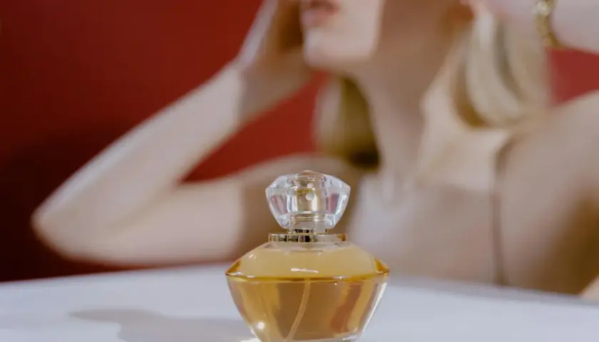 Elegancki flakonik z bursztynowym **attarem** na białym tle, w tle rozmyta postać kobiety.
