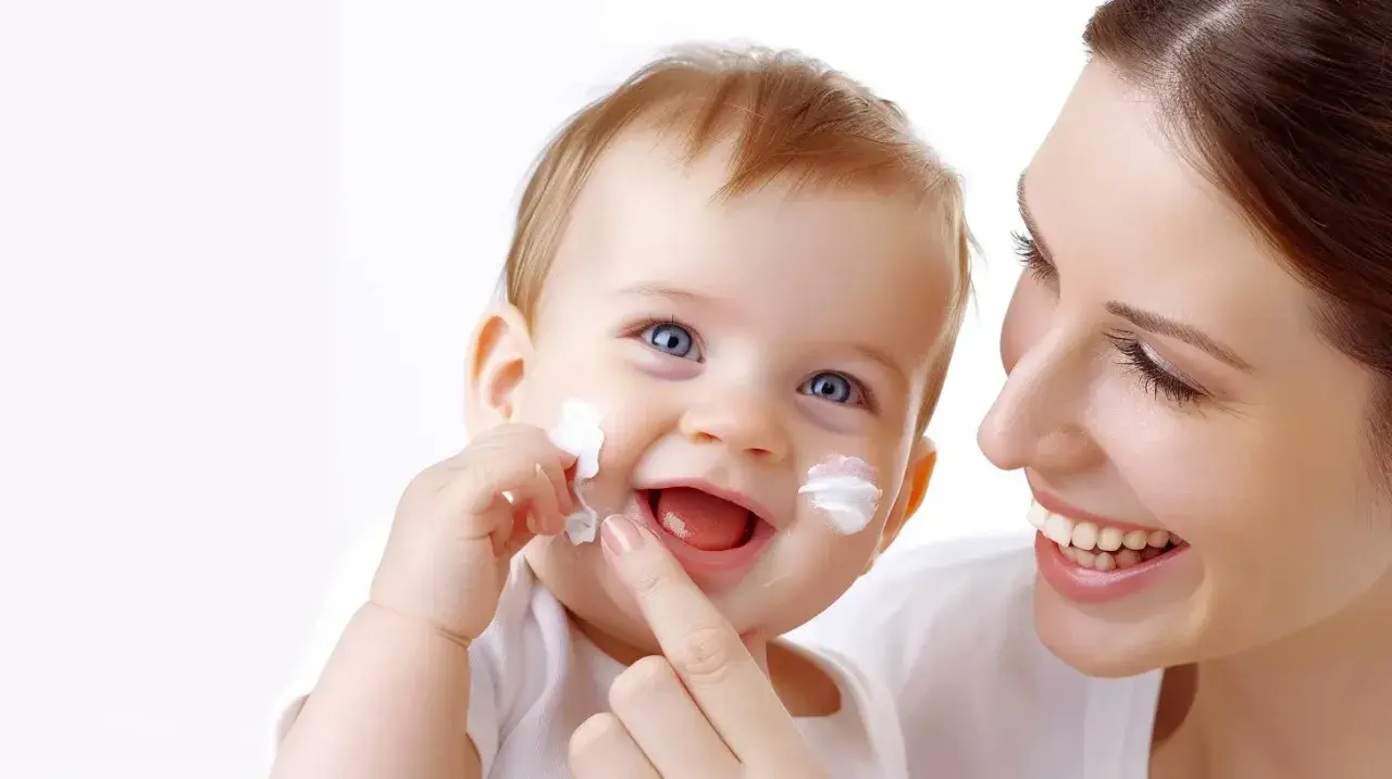 Uśmiechnięte dziecko z białymi plamkami sudocremu na twarzy, mama delikatnie dotyka jego policzka.