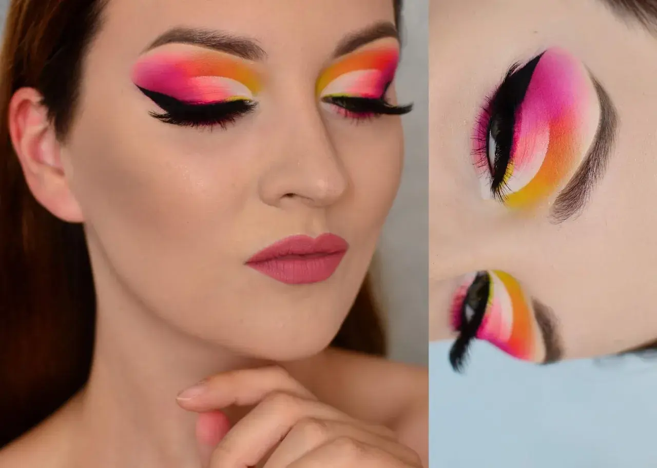 Oczy z wyrazistym makijażem typu cut crease w odcieniach różu, pomarańczy i żółci. Czarne kreski i długie rzęsy podkreślają spojrzenie.